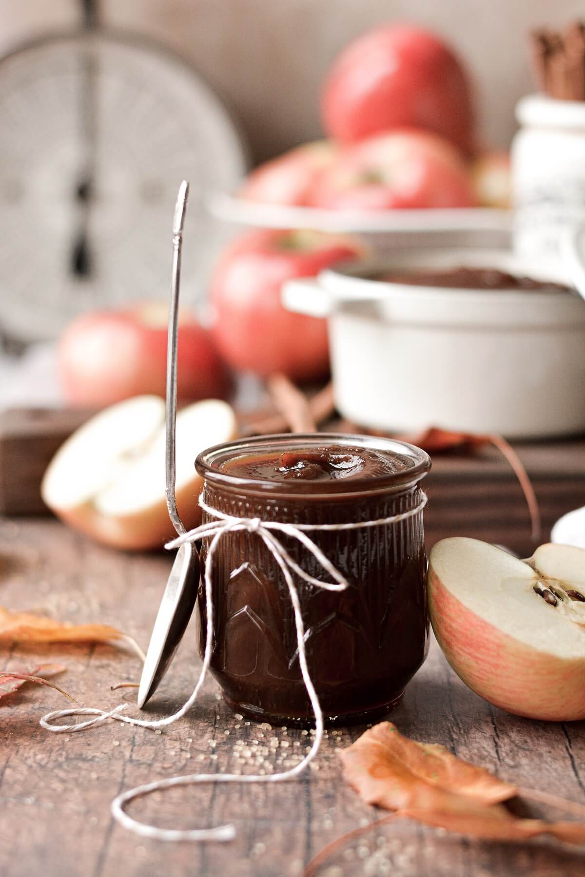 Apple butter in a glass jar, sourrounded by apples and leaves.