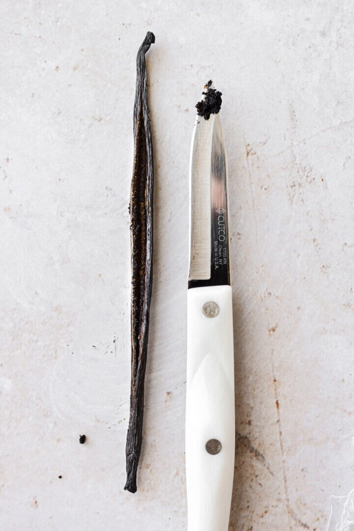 A paring knife next to a split vanilla bean.