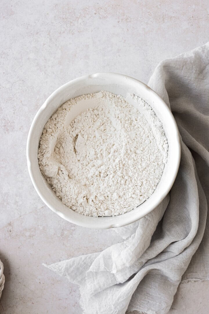 A bowl of flour next to a grey linen.