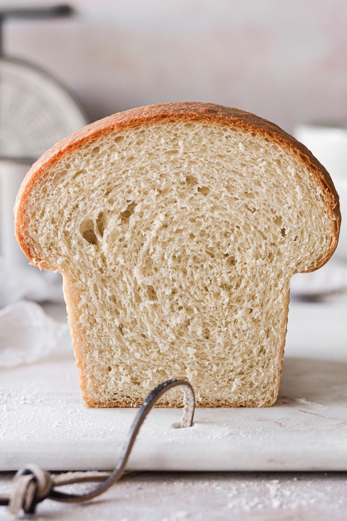 A loaf of homemade white sandwich bread, with a slice cut to show the crumb inside.