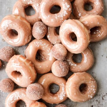 Homemade glazed doughnuts and doughnut holes on a baking sheet.