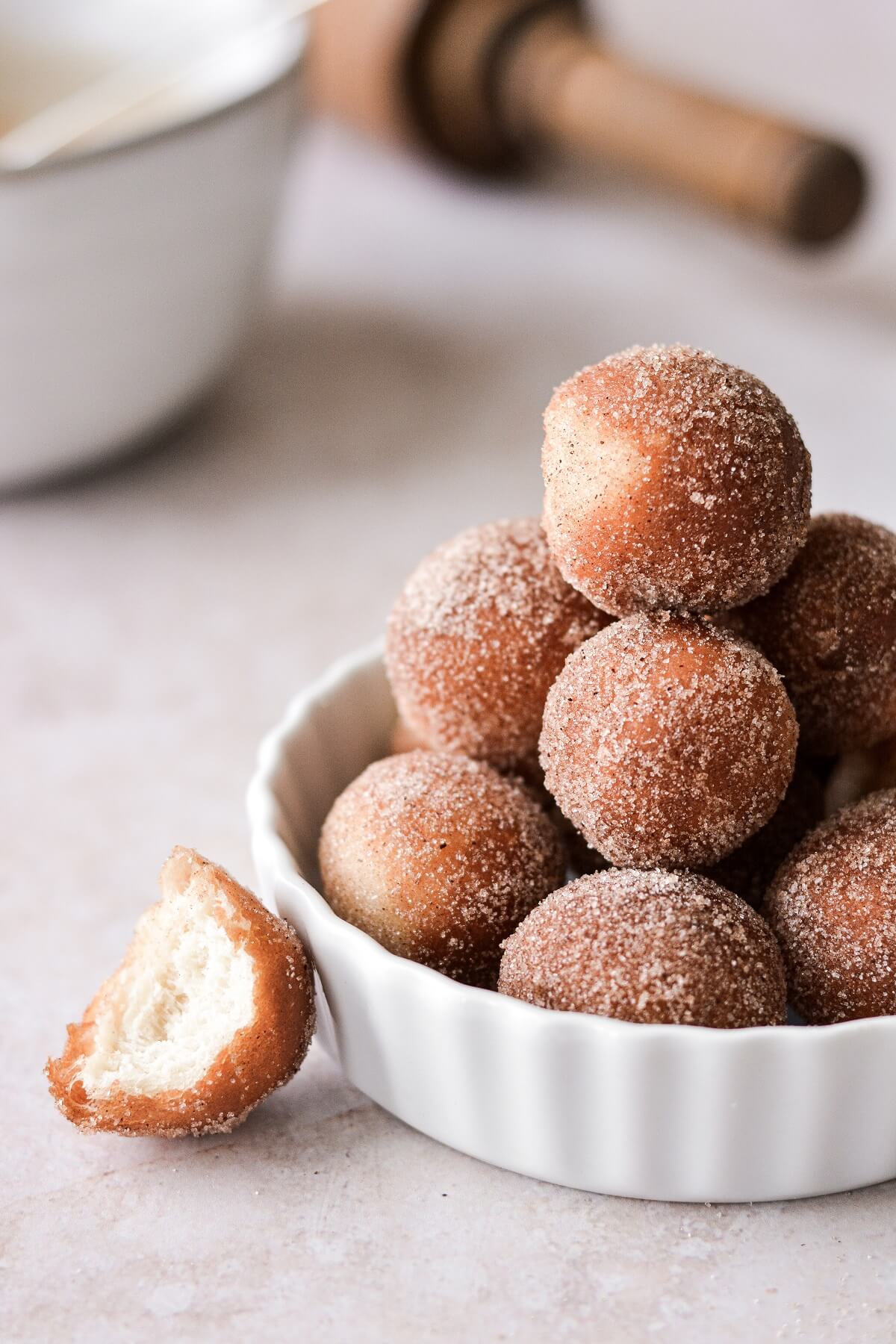 Doughnut holes coated in cinnamon sugar, one with a bite taken.