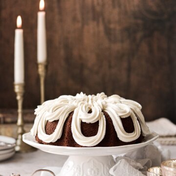 A sweet potato bundt cake decorated with fancy piped cream cheese buttercream, on a white cake stand.
