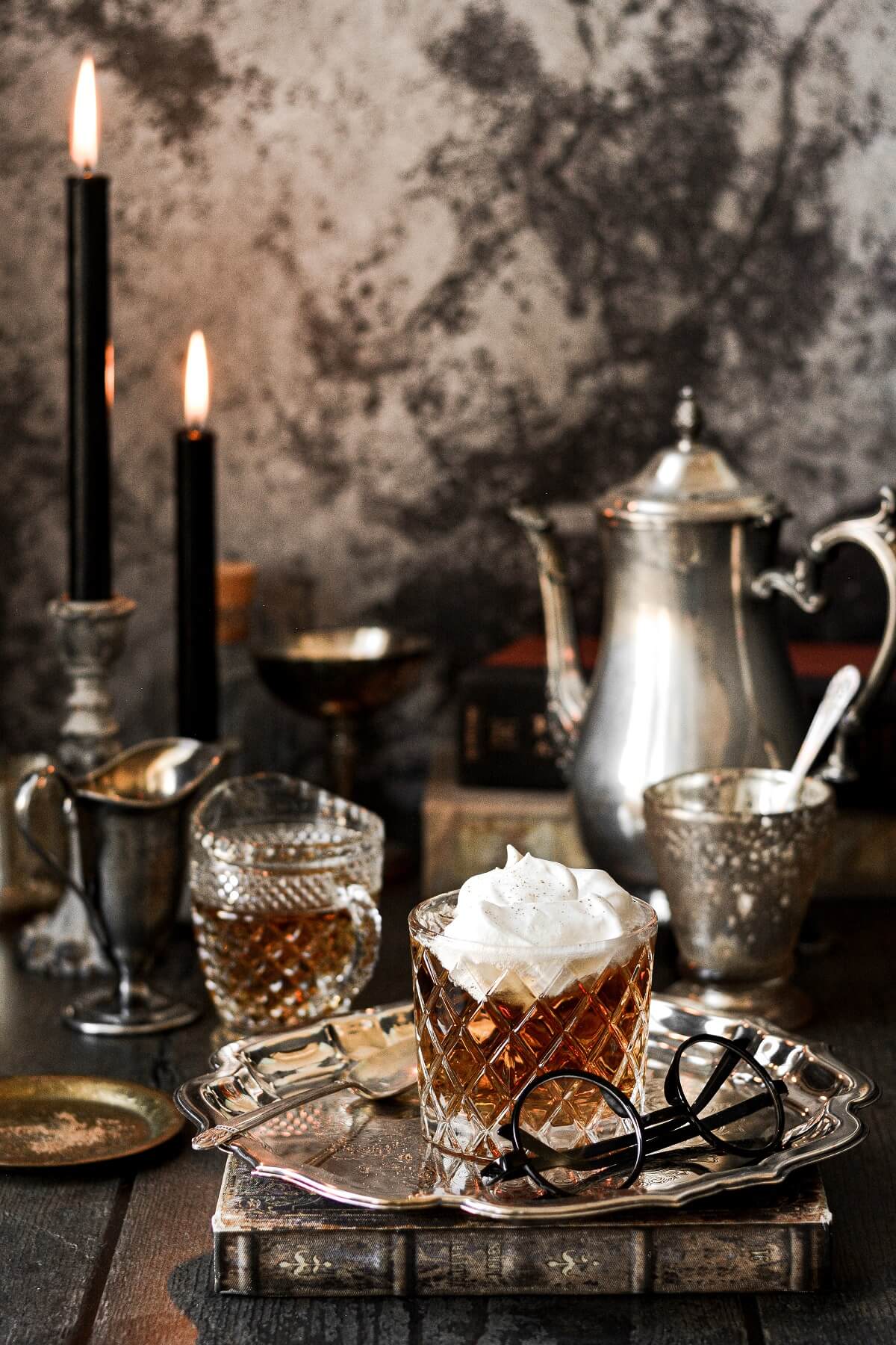 A dark and moody scene with a glass of butter beer, candles, and a silver tea pot.