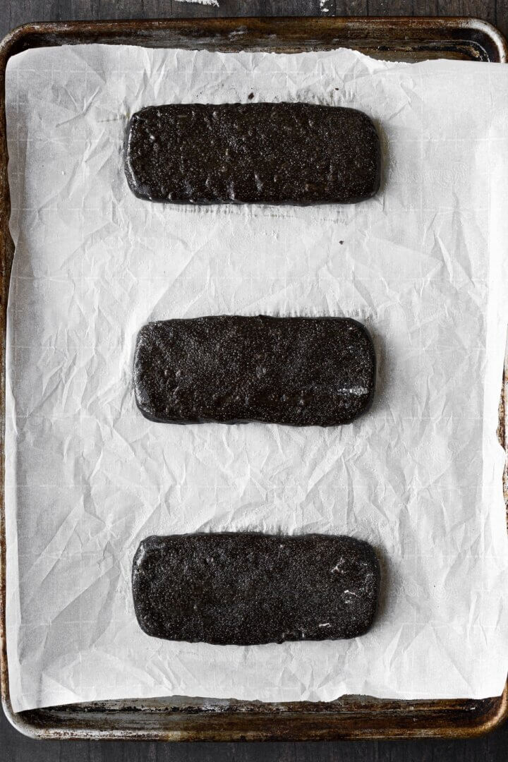 Chocolate biscotti dough shaped into slabs on a baking sheet.