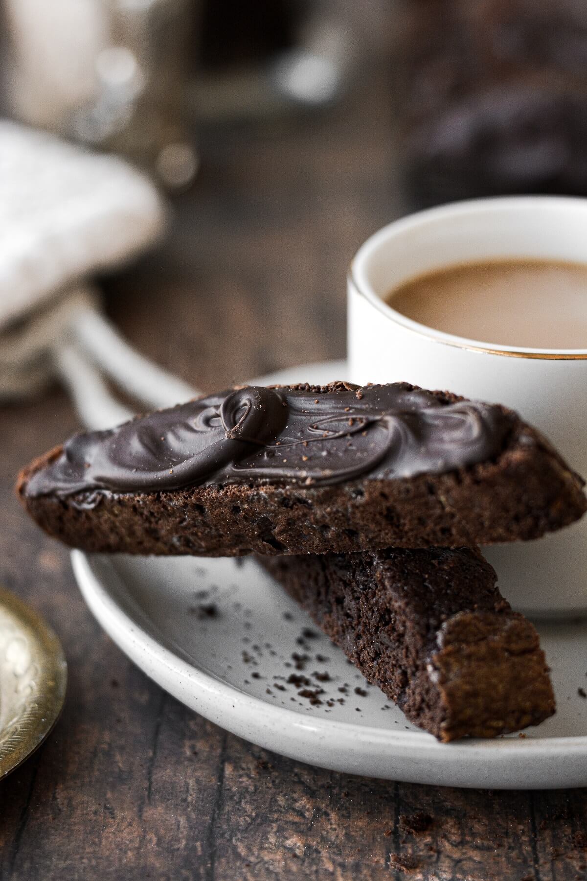 Two chocolate biscotti on a plate with a cup of coffee.