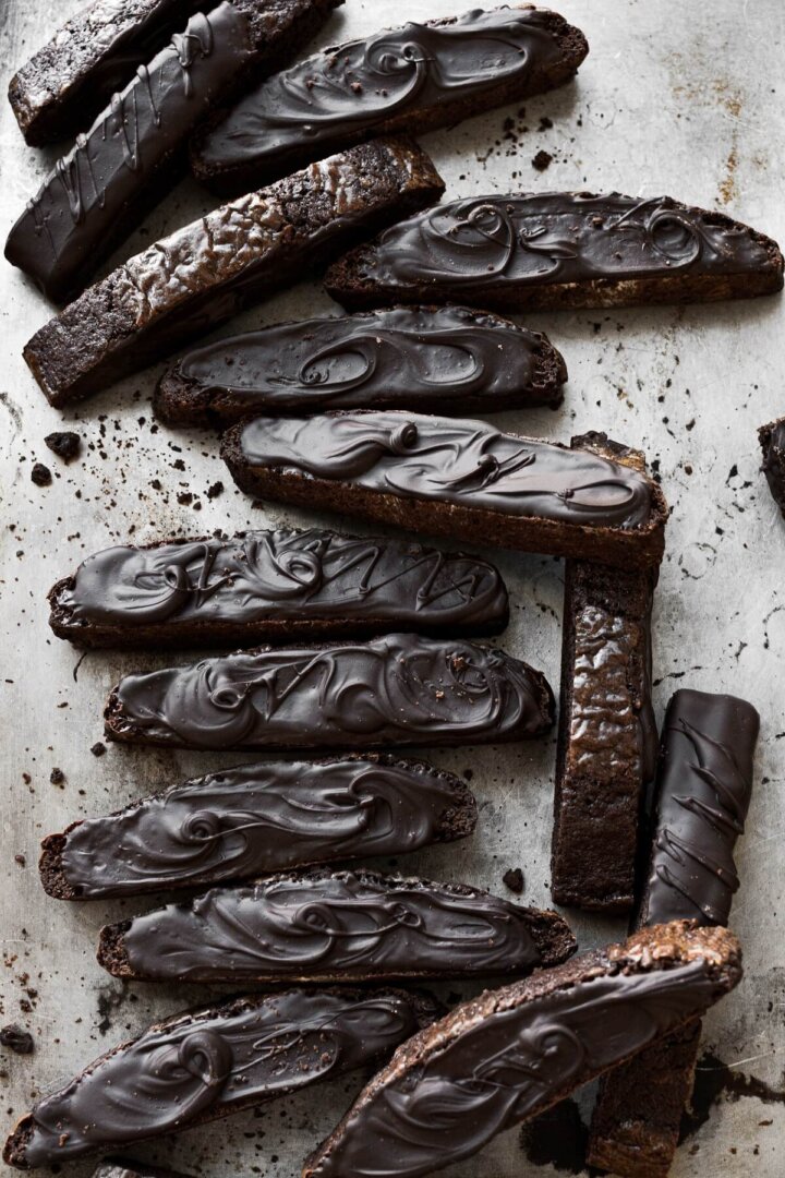 Chocolate biscotti spread with melted chocolate arranged on a baking sheet.