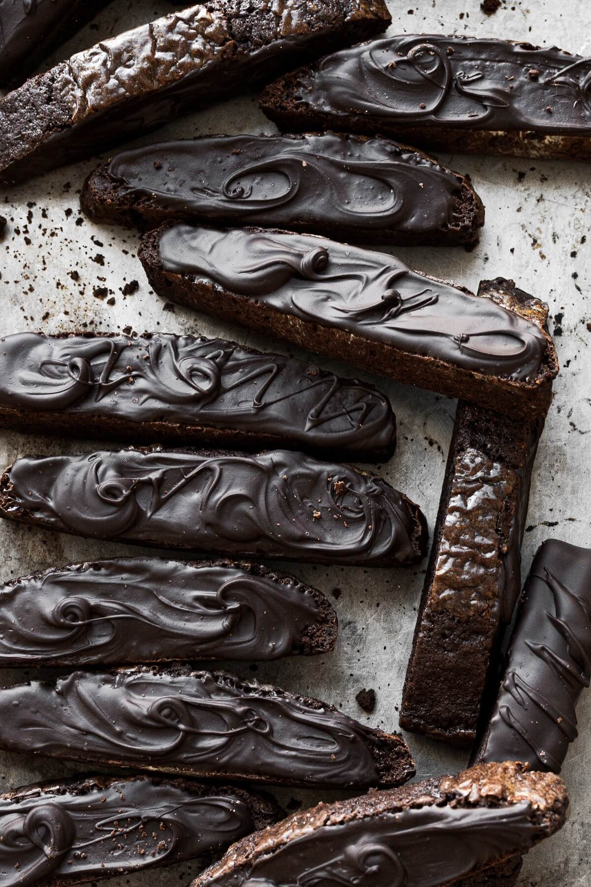 Chocolate biscotti spread with melted chocolate arranged on a baking sheet.