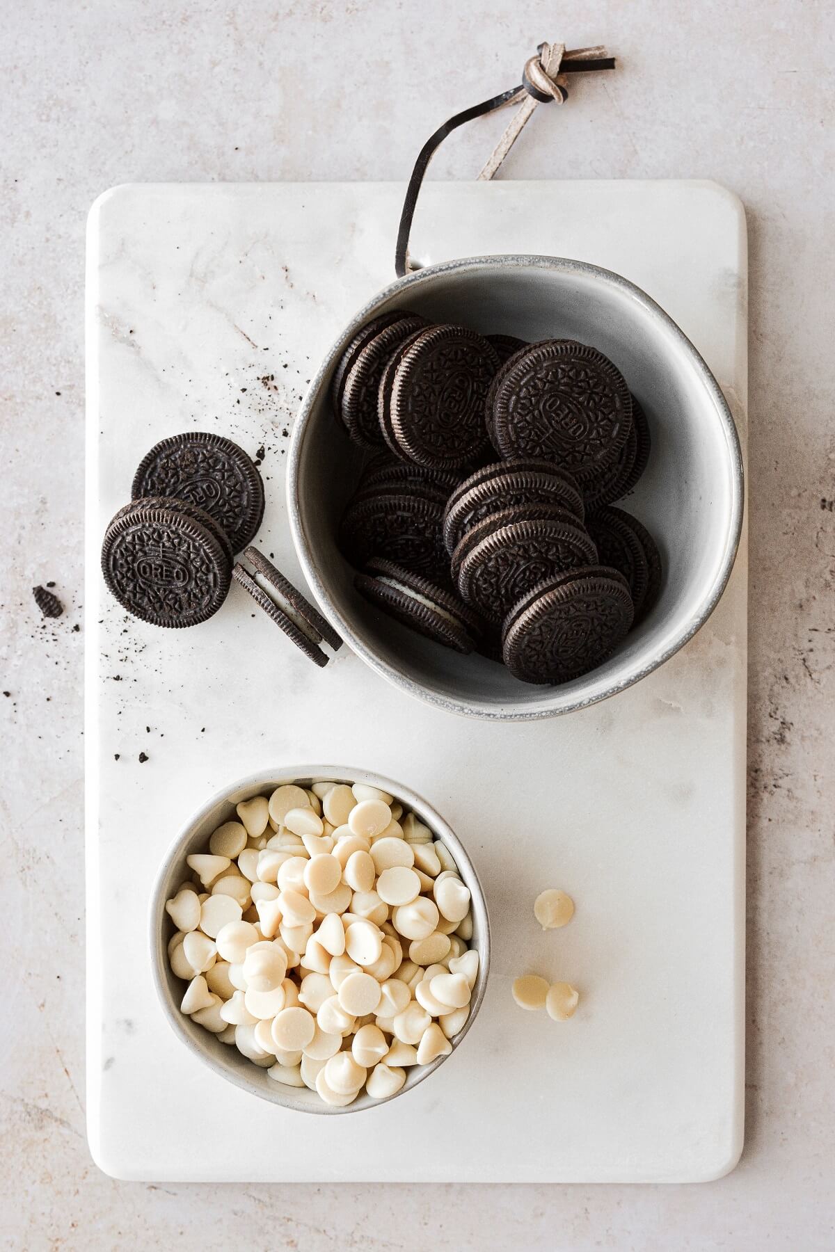 Bowls of Oreos and white chocolate chips on a marble board.
