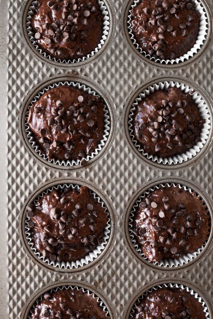 Chocolate muffin batter sprinkled with chocolate chips in a muffin pan.