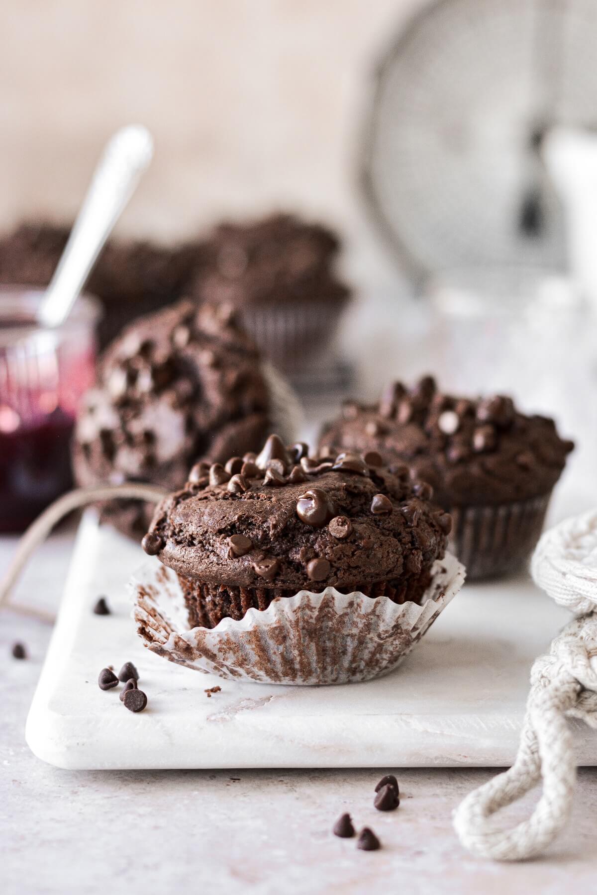 Double chocolate muffins sprinkled with chocolate chips on a white serving board.