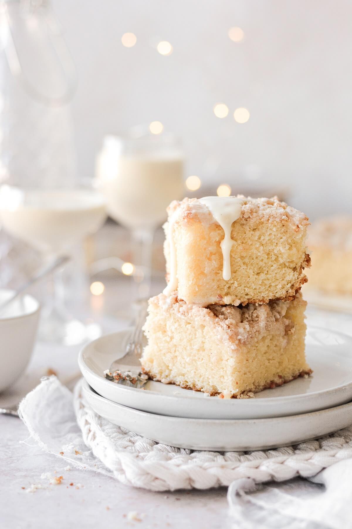 Two squares of eggnog coffee cake, stacked on a plate, with icing dripping down.