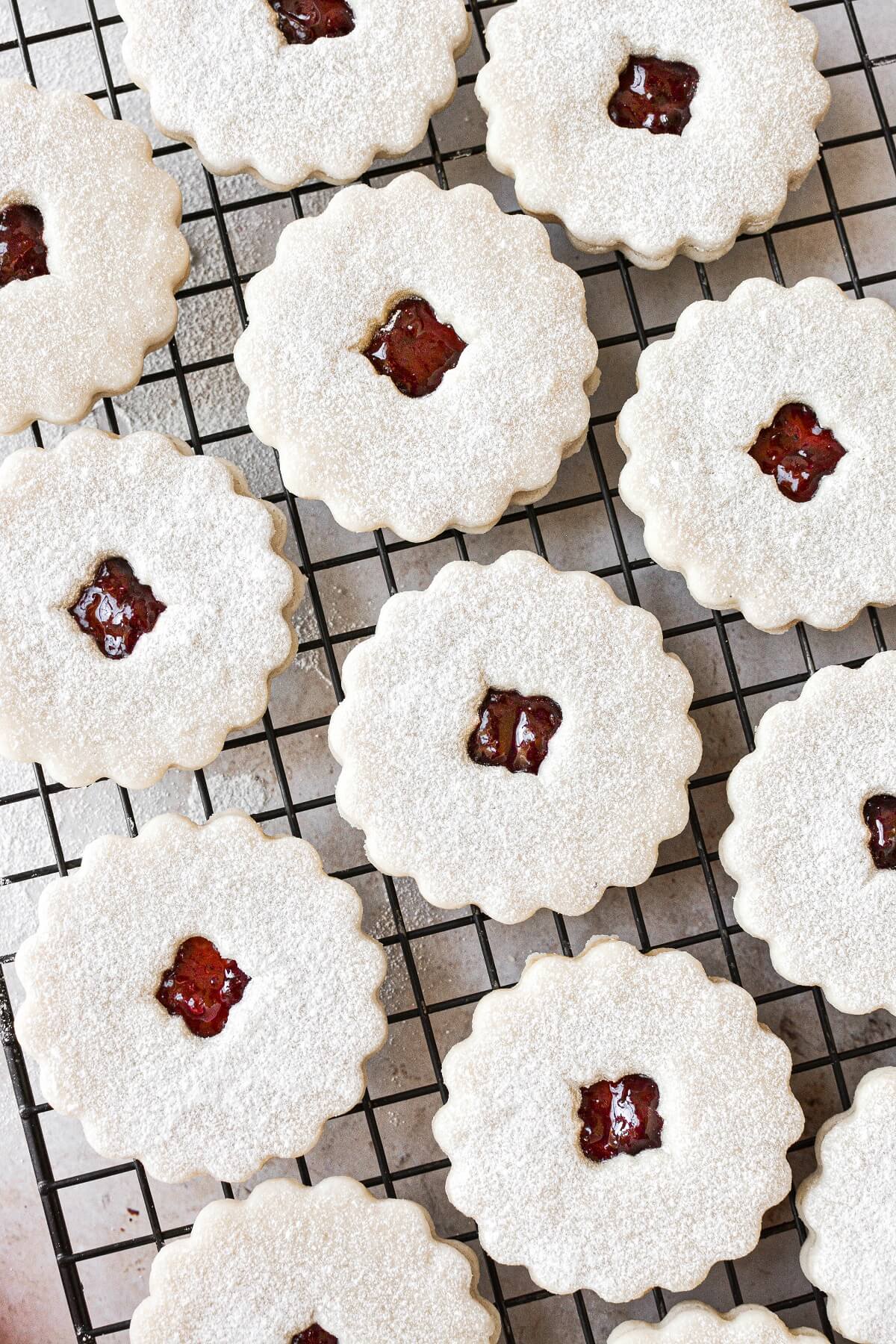 Linzer cookies filled with cherry jam, arranged on a black cooling rack.