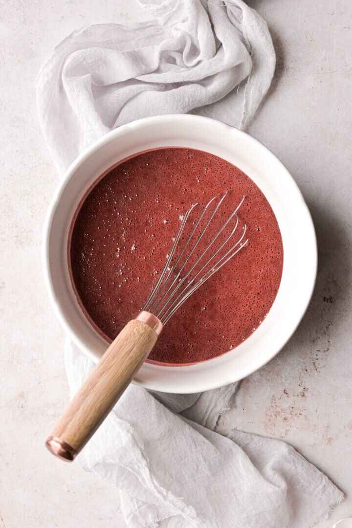 A bowl of red velvet cake batter with a whisk.