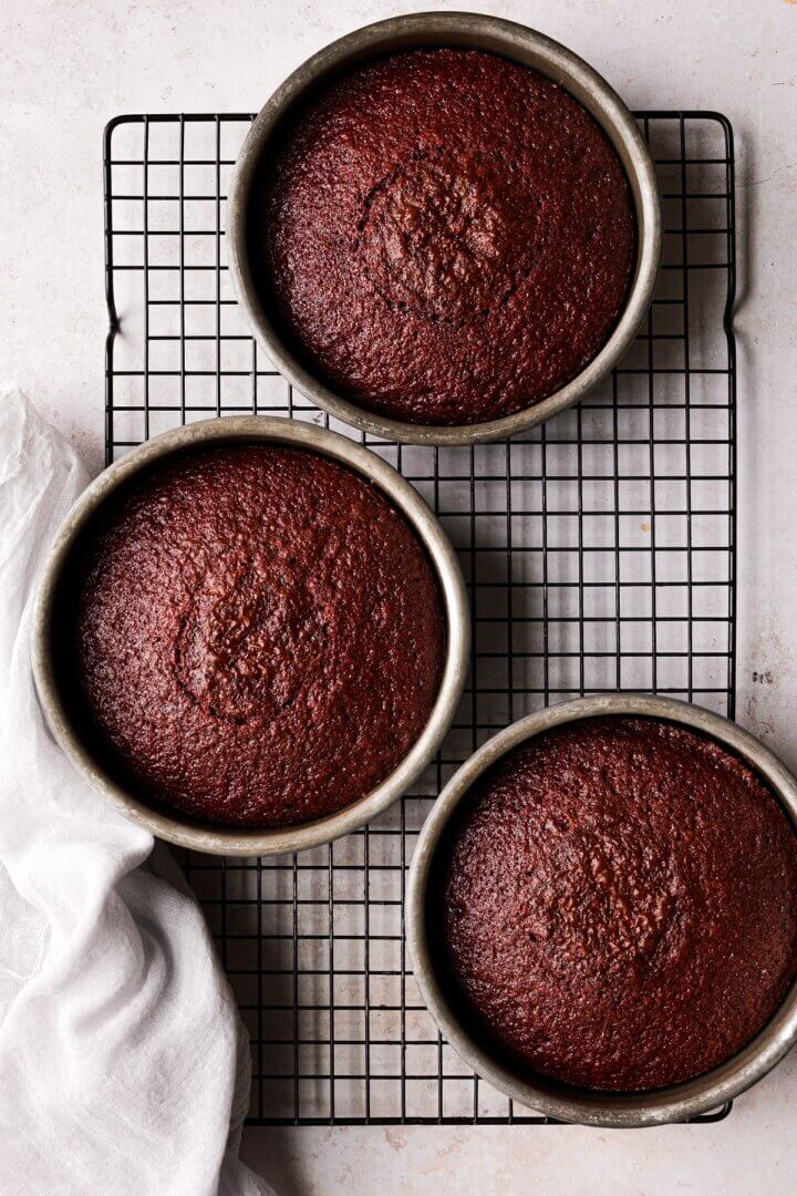 Red velvet cake in three cake pans sitting on a cooling rack.