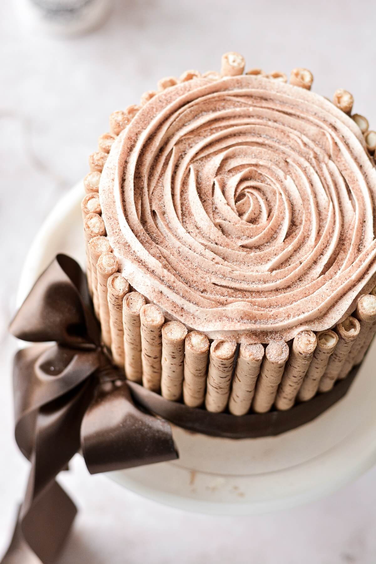 A snickerdoodle cake with piped buttercream, surrounded by Pirouettes cookies and tied with a brown satin ribbon.