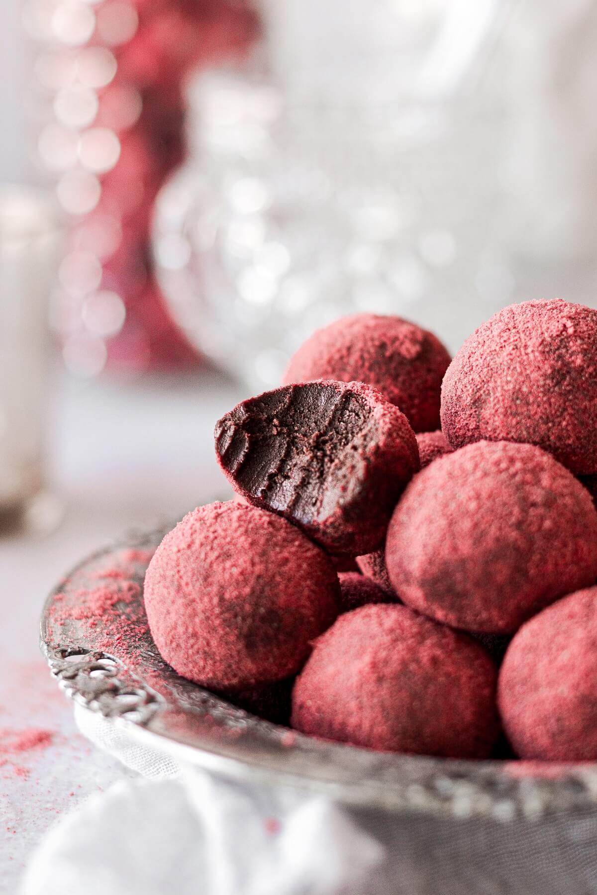 A silver bowl of chocolate strawberry truffles, one with a bite taken.