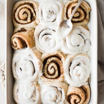 Just baked cinnamon rolls being spread with vanilla icing.