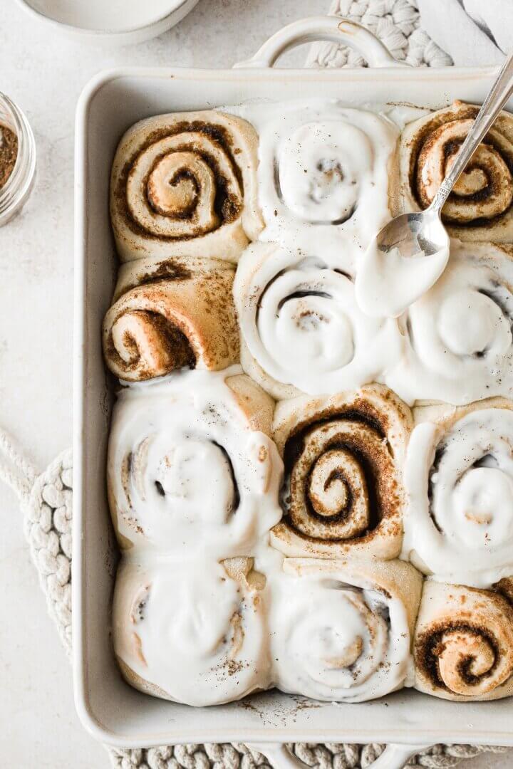 Just baked cinnamon rolls being spread with vanilla icing.
