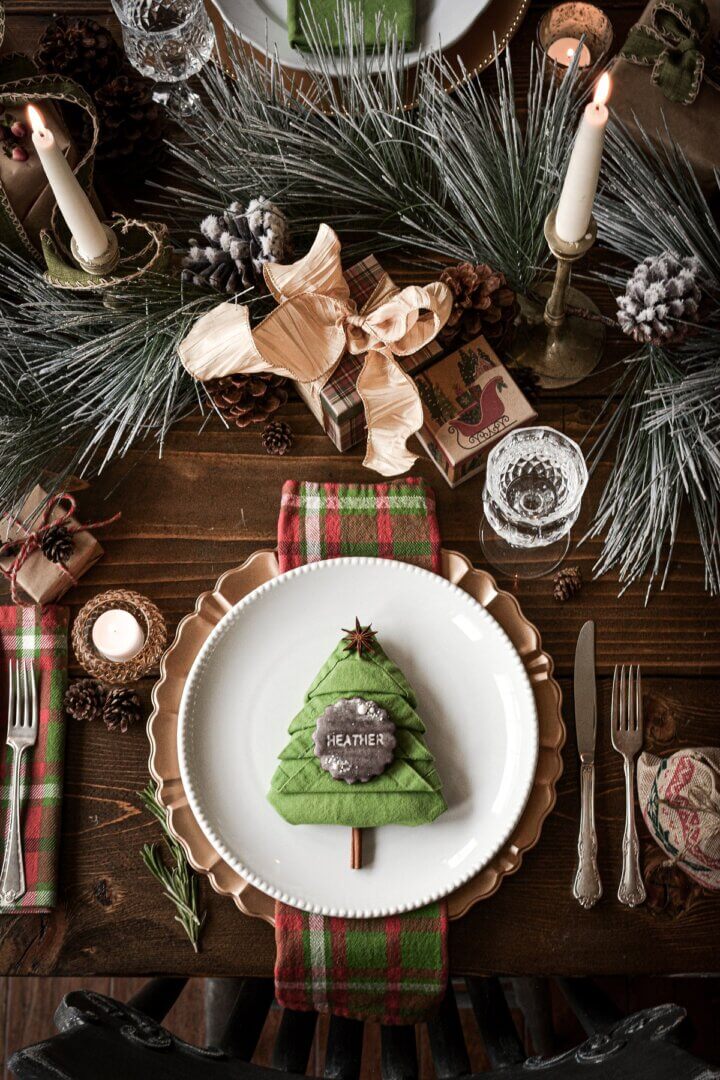 A Christmas place setting with a chocolate cookie stamped with the name "Heather" sitting on green napkin folded like a Christmas tree..