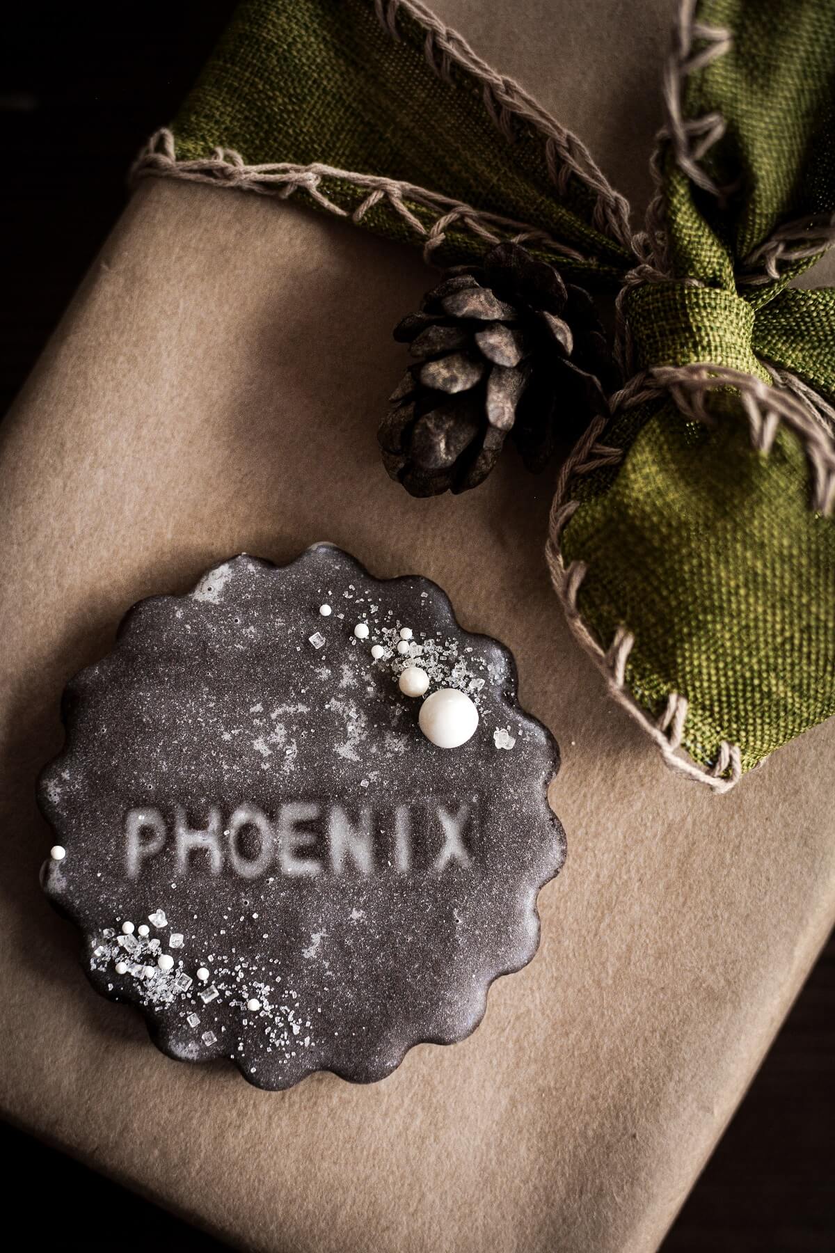 A chocolate place card cookie stamped with the name "Phoenix" sitting on top of a Christmas present.