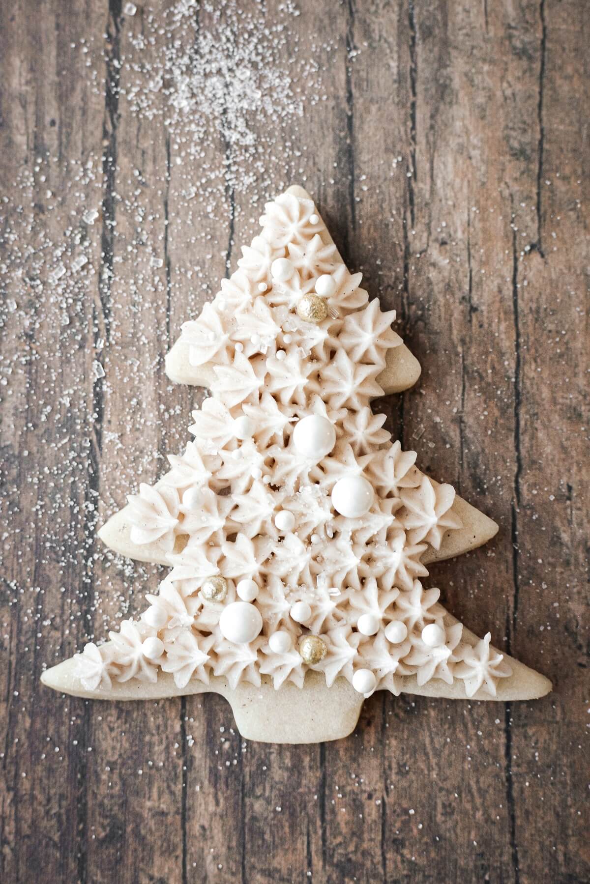 A Christmas tree cookie with buttercream piped in stars and decorated with sugar pearls.