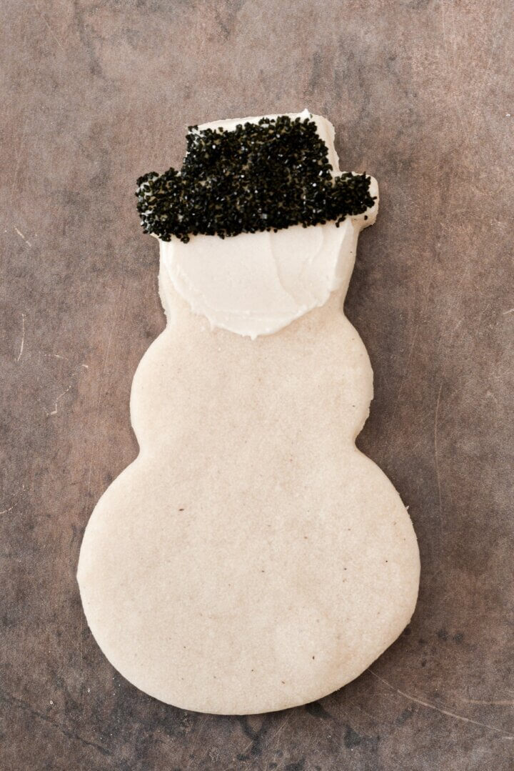 A snowman cookie spread with buttercream and a black sugar hat.