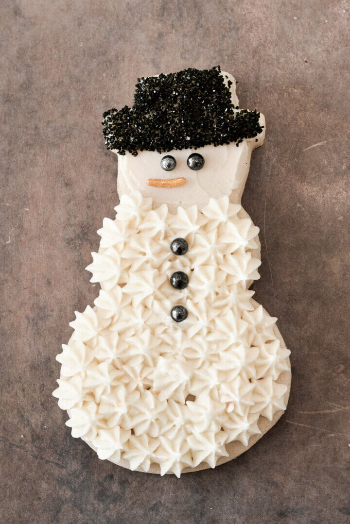 A snowman sugar cookie frosted with buttercream and sugar pearls.