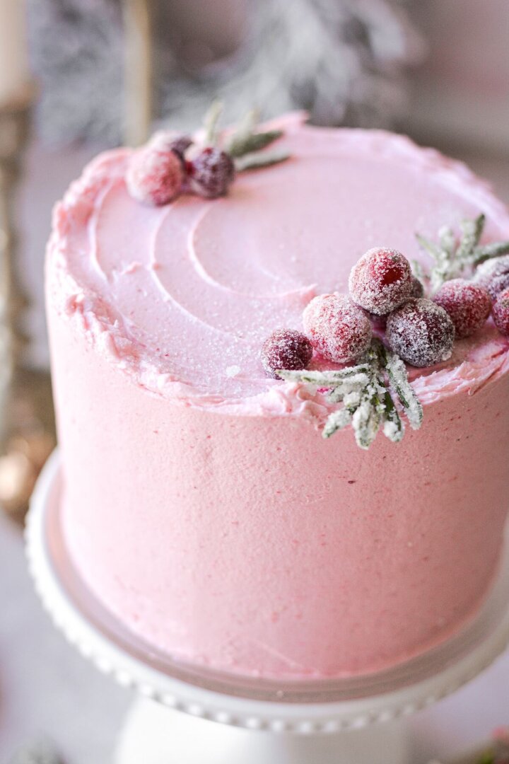 Cranberry cake with pink buttercream decorated with sugared cranberries and rosemary.