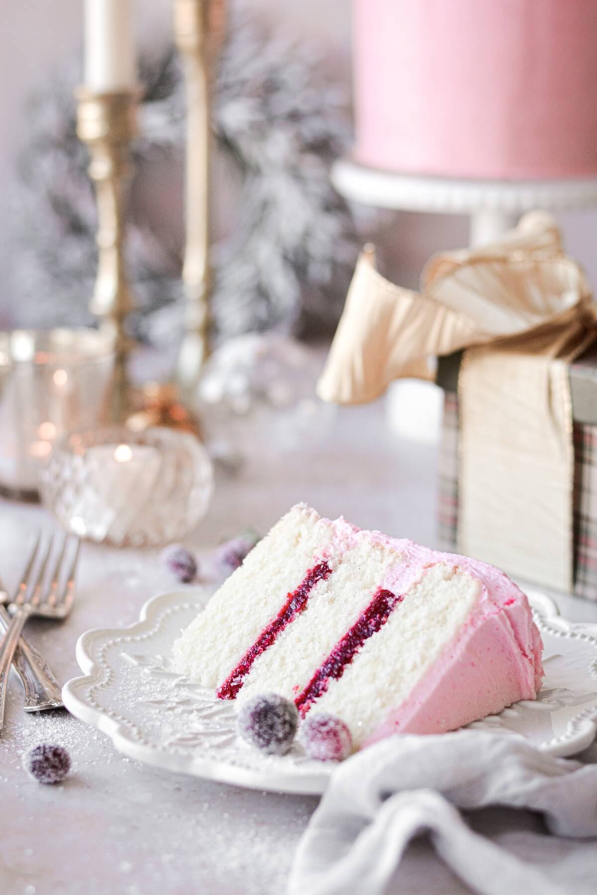 A slice of cranberry cake with presents and candles in the background.