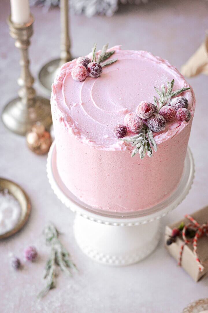 Cranberry cake with pink buttercream decorated with sugared cranberries and rosemary.