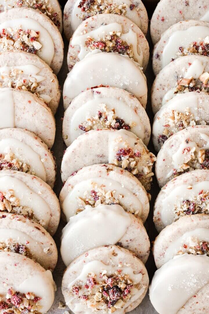 Cranberry pecan shortbread cookies with orange icing and sprinkled with candied orange peel.