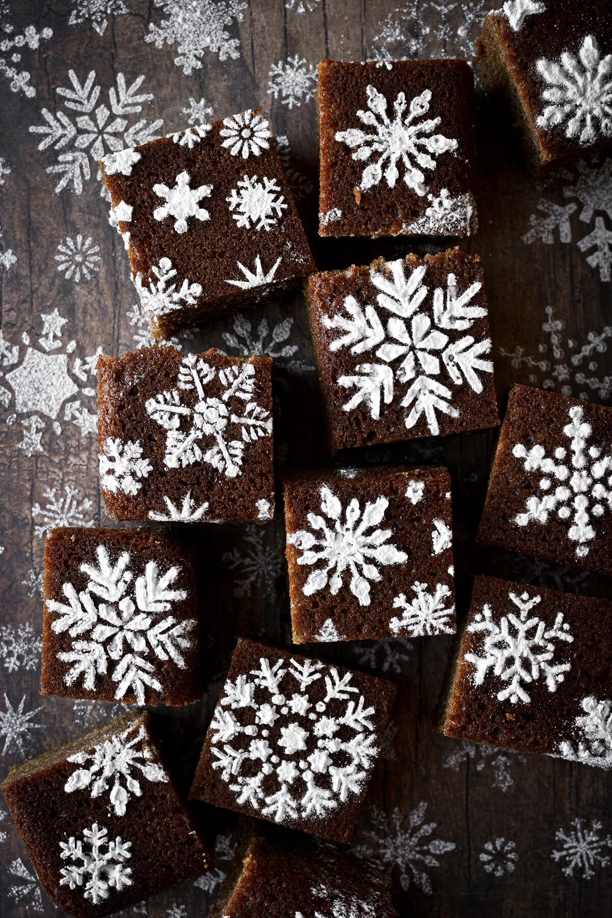 Gingerbread sheet cake cut into squares and decorated with powdered sugar snowflake stencils.