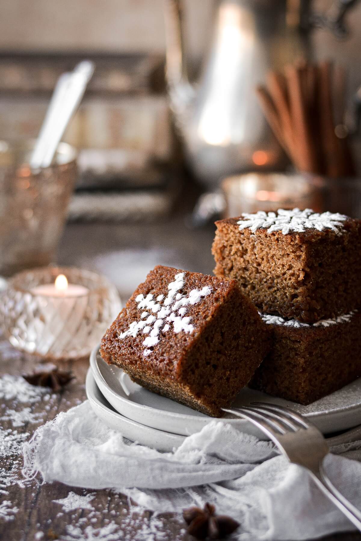 Squares of gingerbread sheet cake with powdered sugar snowflake stencils on a plate.
