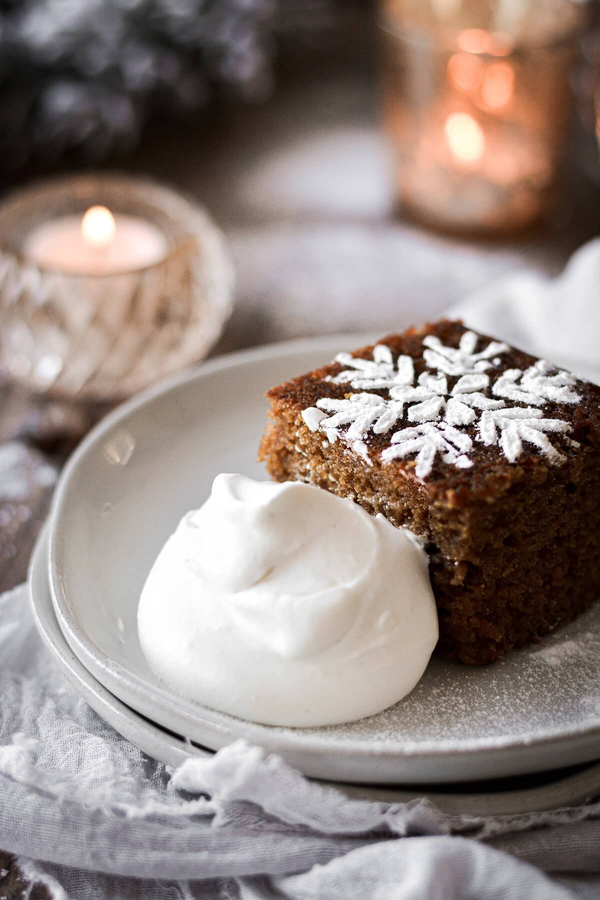 A piece of gingerbread cake with a powdered sugar snowflake, served with whipped cream.