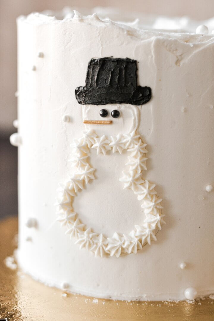 A partially finished snowman design on a layer cake.