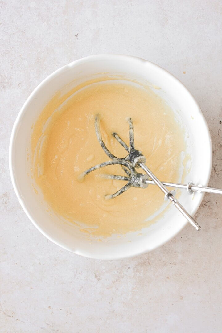 A mixture of egg yolks, sugar and butter whisked together in a bowl.