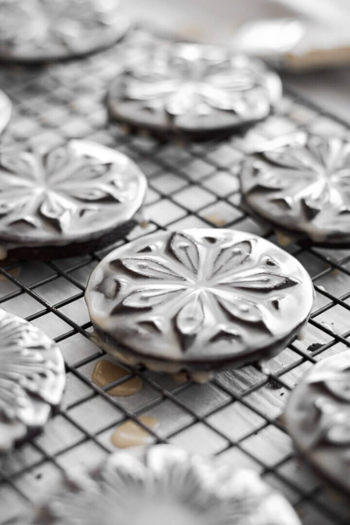 Stamped chocolate shortbread cookies glazed with icing on a black cooling rack.