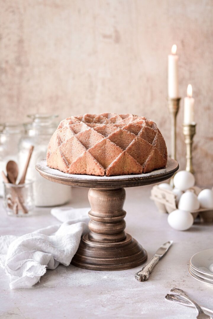 Vanilla bean cream cheese pound cake dusted with powdered sugar on a wooden cake stand.