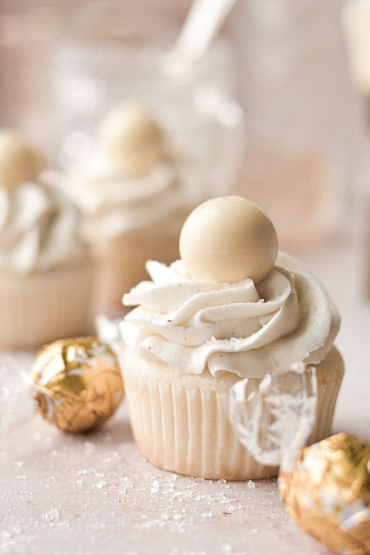 White velvet cupcakes topped with white chocolate truffles, surrounded by truffles in gold wrappers.
