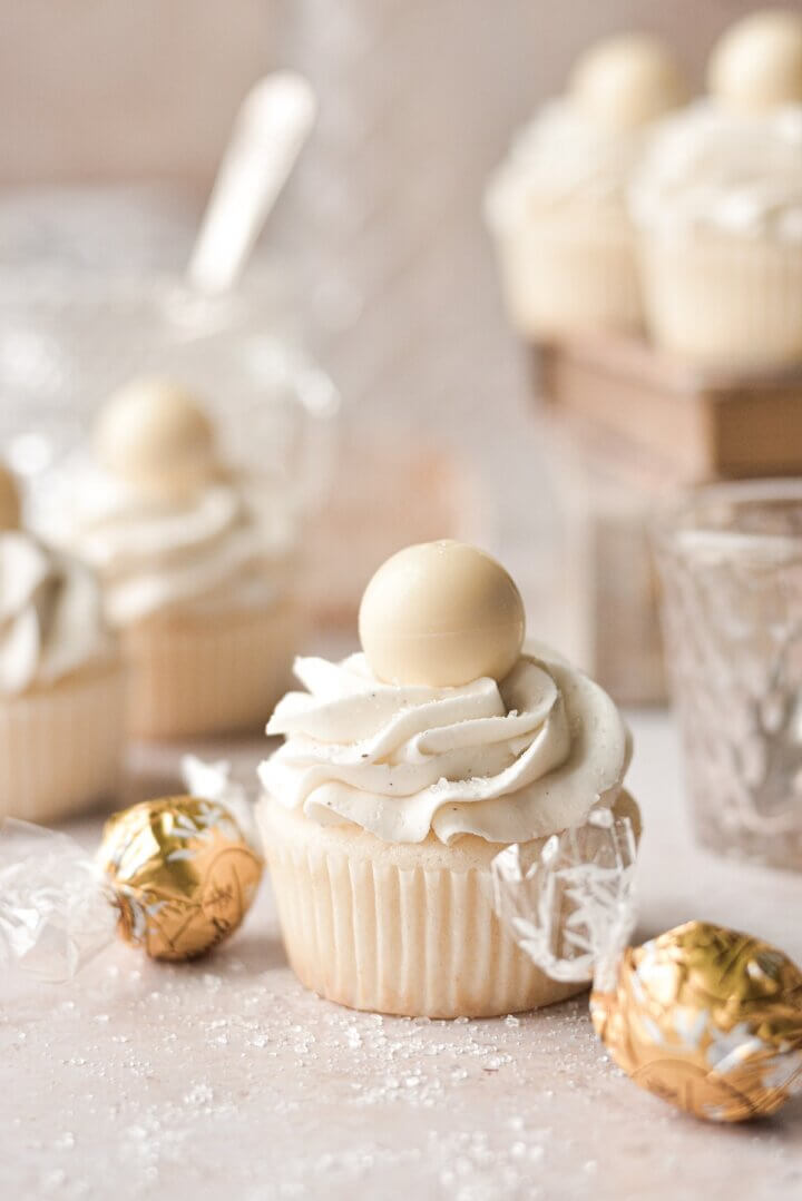 White velvet cupcakes topped with white chocolate truffles, surrounded by truffles in gold wrappers.