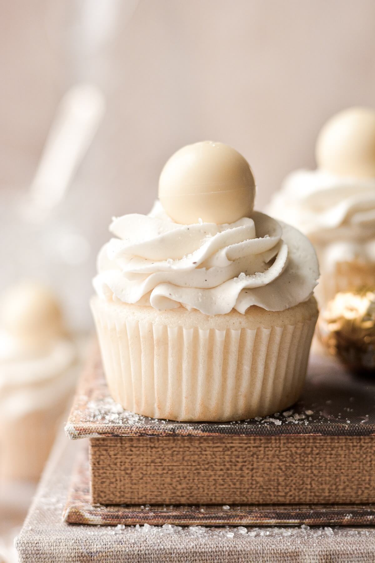 A white velvet cupcake topped with a white chocolate truffle, sitting on top of a book.