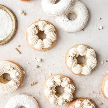 Baked vanilla cake doughnuts with piped buttercream and gold and white sprinkles.