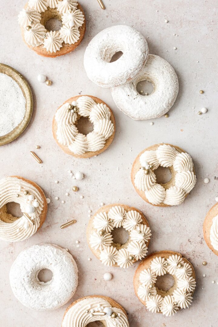 Baked vanilla cake doughnuts with piped buttercream and gold and white sprinkles.