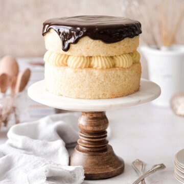 Boston cream pie on a marble and wood cake stand.