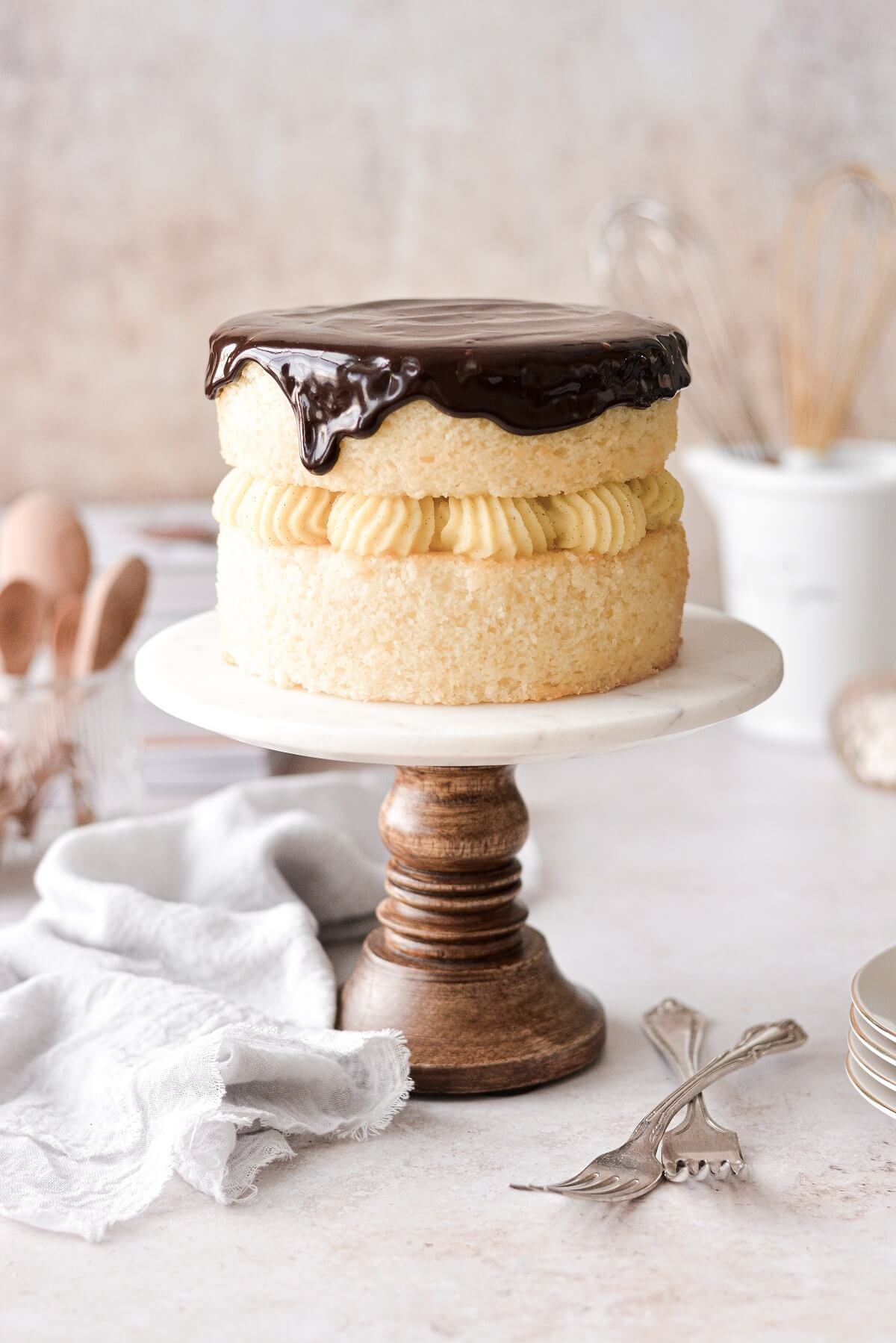 Boston cream pie on a marble and wood cake stand.