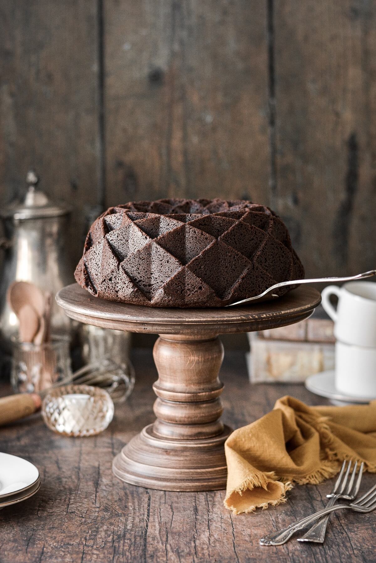 A chocolate bundt cake on a wooden cake stand.