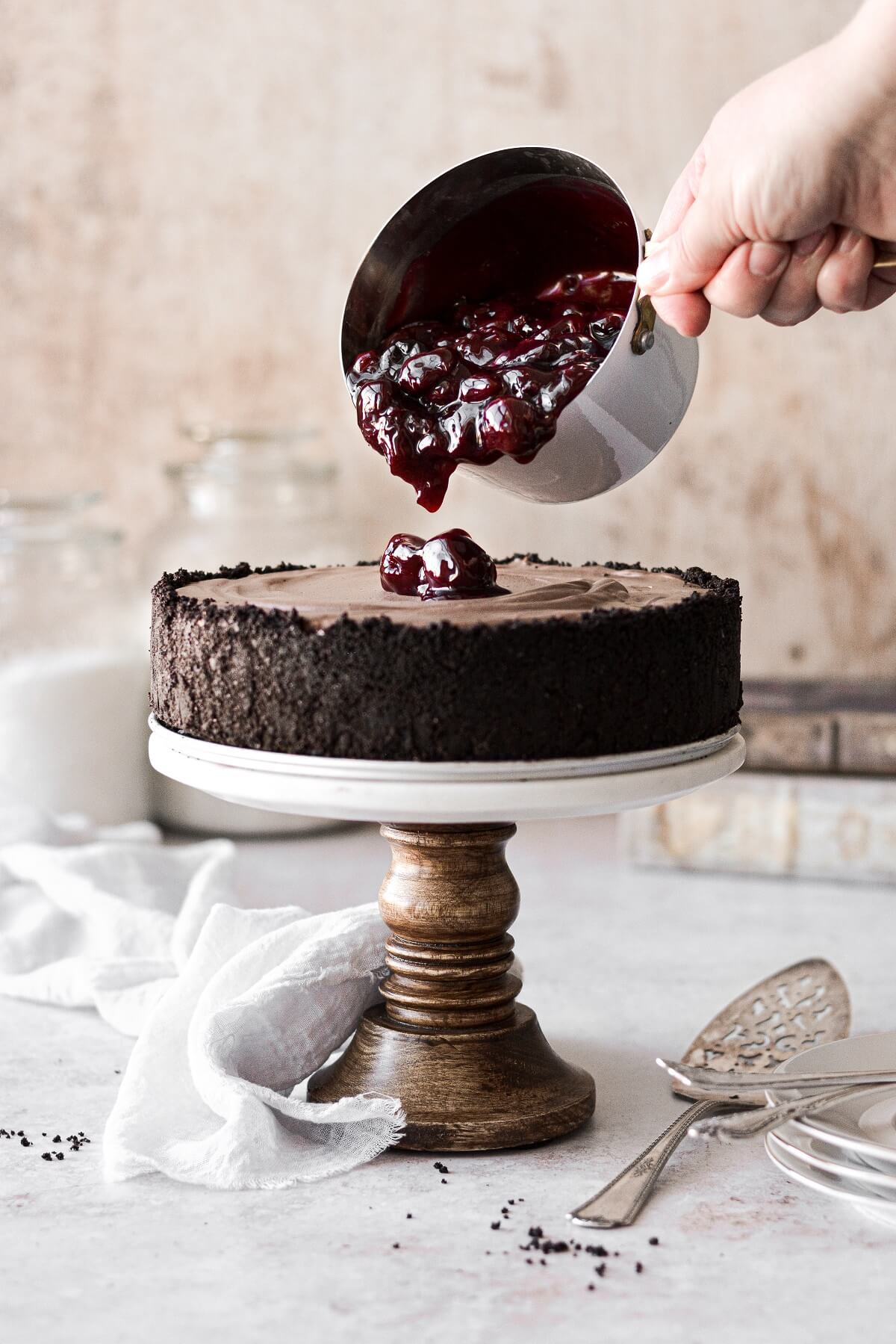 Cherry sauce being poured on top of a chocolate cheesecake.
