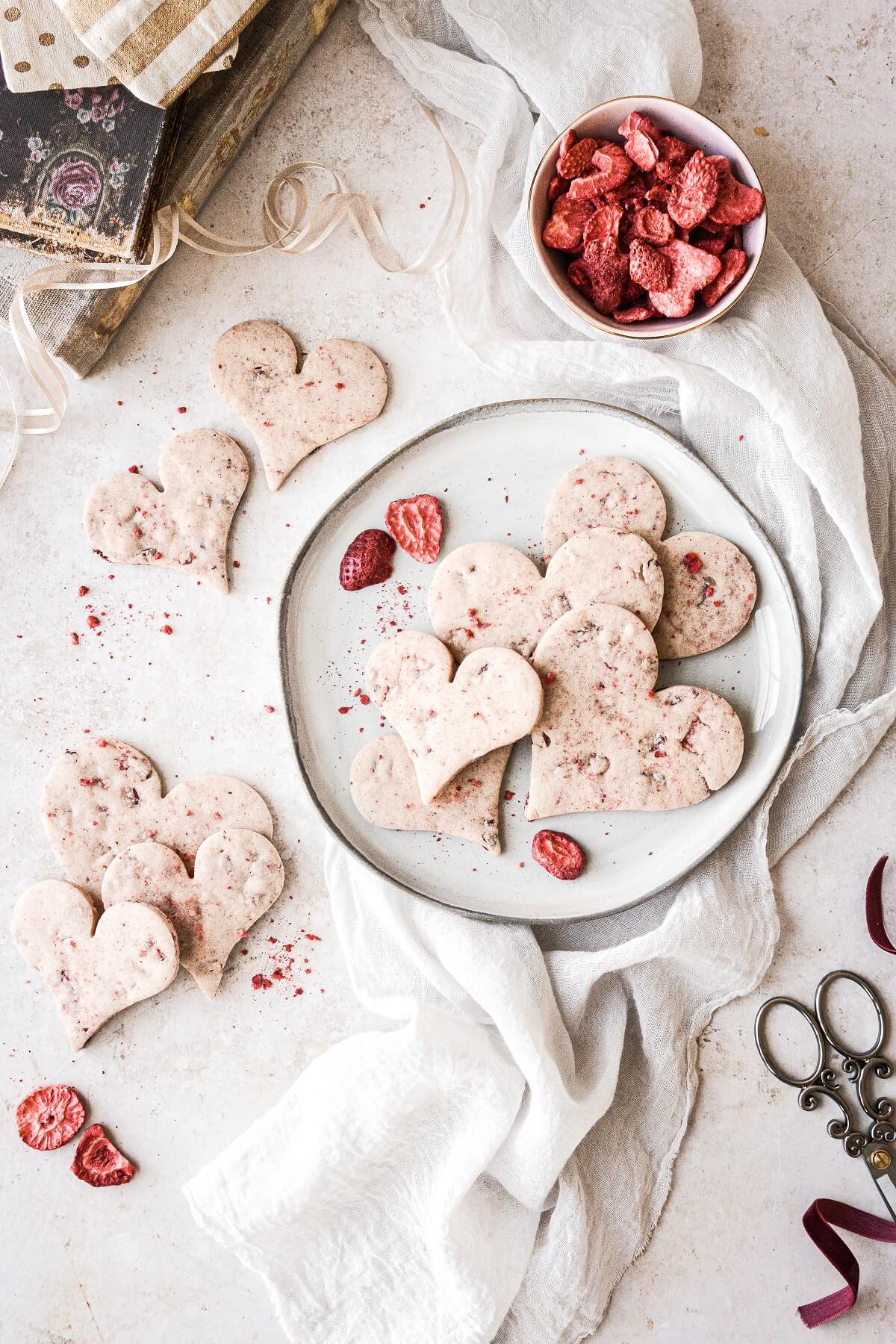 Heart shaped strawberry shortbread cookies next to a bowl of freeze dried strawberries.