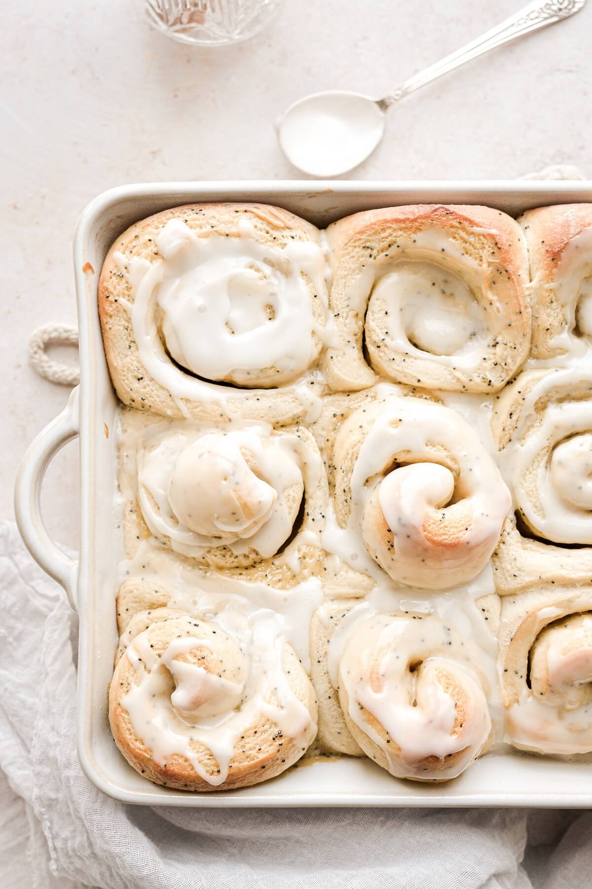 Lemon poppy seed rolls in a baking dish drizzled with lemon icing.